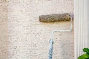 Paint roller attached to pole on outside wall of house