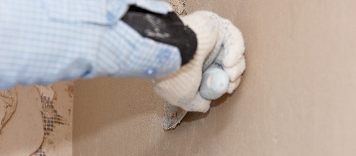Hand with a spatula in the process of leveling the raw plaster.