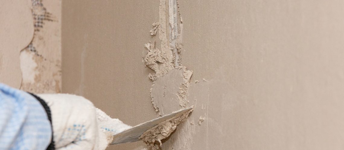Hand with a spatula in the process of leveling the raw plaster.